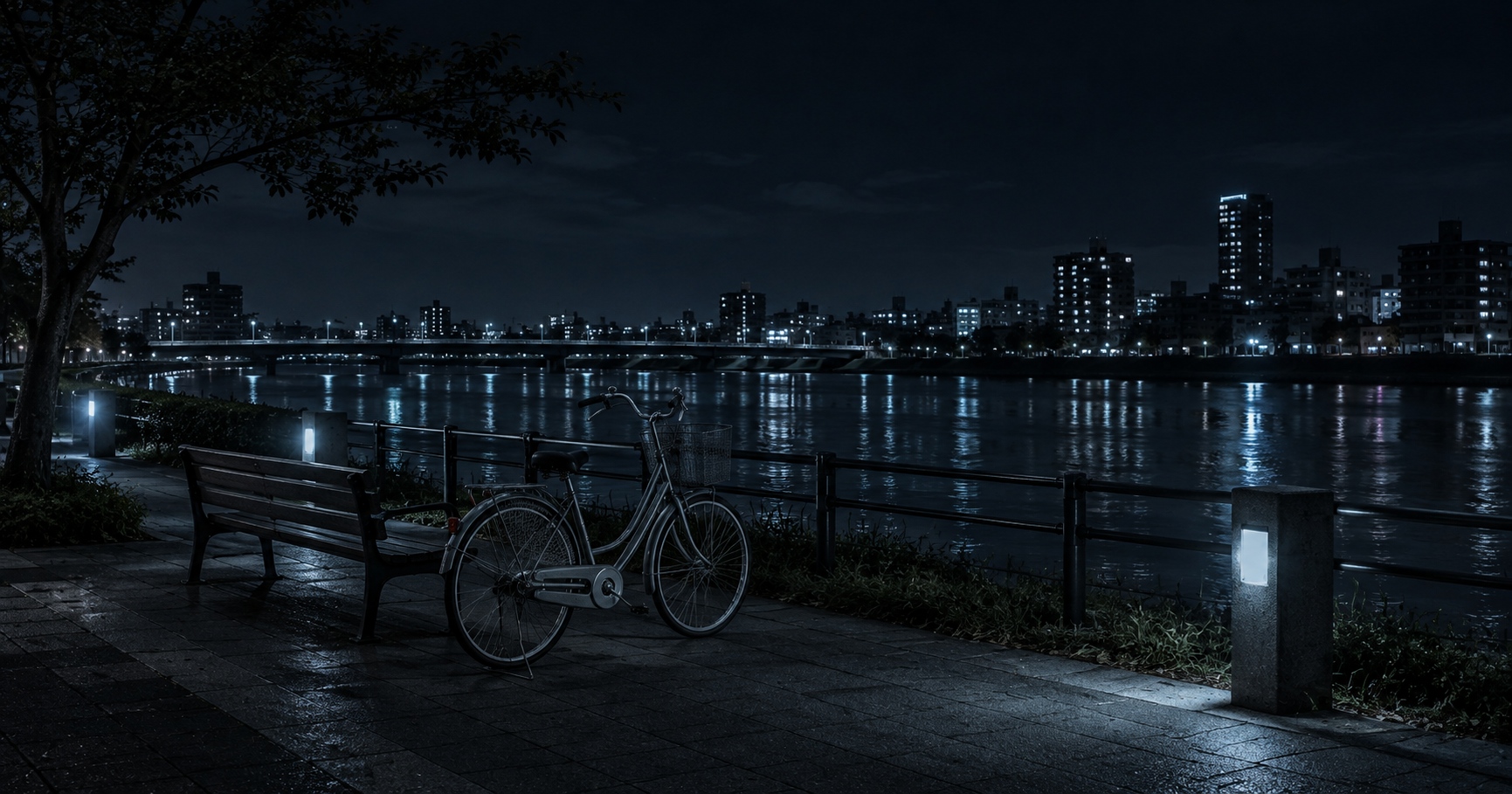 青白い光が差す夜の川沿いに停めた自転車とベンチ